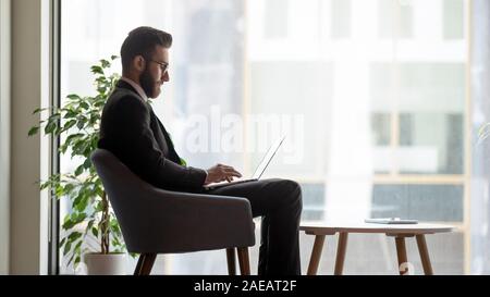 Grave imprenditore arabo occupato con computer portatile in ufficio Foto Stock