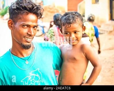 PUDUCHERRY, INDIA - dicembre circa, 2018. Unidentified affettuoso orgoglioso giovane azienda il suo figlio in armi per la strada del villaggio, sorridente a t Foto Stock