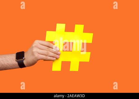 Primo piano della mano maschio con orologi da polso azienda grande giallo hashtag segno, tempo per virale delle sfide e delle tendenze nei social media, internet blogging ind. Foto Stock