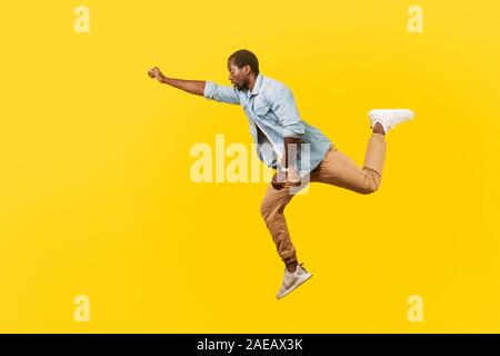 A piena lunghezza Ritratto di grave cool uomo bello in denim Camicia casual salti in aria o volare alto con un braccio teso, la sensazione di essere superman. Foto Stock