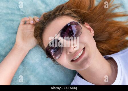 Ritratto di giovane ragazza adolescente in occhiali da sole che stabilisce sul panno blu sullo sfondo. Foto Stock