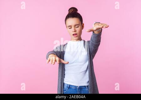 La cecità. Ritratto di bruna ragazza adolescente con bun hairstyle in abiti casual in piedi con gli occhi chiusi, disorientati raggiungendo le mani per trovare wa Foto Stock