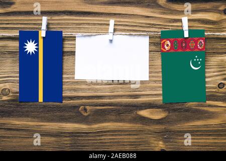 Appendere bandiere di Nauru e Turkmenistan attaccata alla corda con vestiti perni con copia spazio bianco sulla nota carta su sfondo di legno.Diplomatic relatio Foto Stock