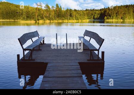 Dock o il molo sul lago nel giorno d'estate. Passerella vuota con due panche in Bielorussia Foto Stock