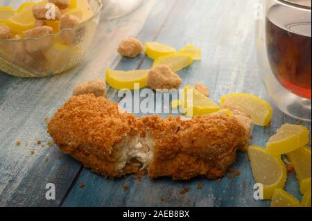 Uno rotto torta, un bicchiere di tè nero, pezzi di zucchero di canna e marmellata fette di limone su un sfondo di legno Foto Stock