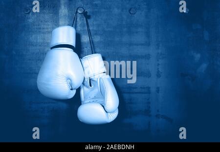 Vicino la coppia di classico bianco pelle i guantoni appesi sopra blu scuro muro con spazio di copia Foto Stock