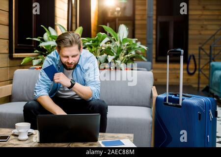 Uomo Felice Tiene un passaporto in corso di validità e di utilizzo del portatile per prenotazione camere e biglietti prima di un lungo viaggio in arrivo. Foto Stock