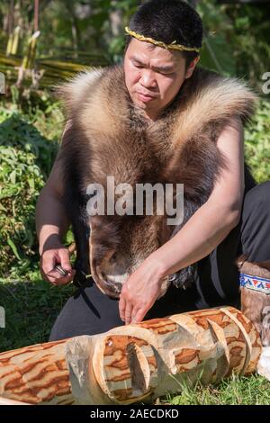Itelmens nazionale festival rituale Alhalalalay, uomo in abbigliamento tradizionale popolazioni indigene della penisola di Kamchatka scolpisce idolo faccia con il coltello Foto Stock