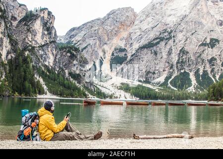 Giovane turista escursionista uomo ascoltare musica seduto da lago alpino Lago di Braies (Lago di Braies) in Trentino, Dolomiti, Italia. Foto Stock