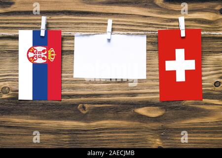 Appendere bandiere di Svizzera e Serbia attaccata alla corda con vestiti perni con copia spazio bianco sulla nota carta su sfondo di legno.Diplomatic relatio Foto Stock