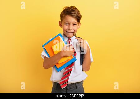 Bambino piange perché ha un sacco di compiti di scuola. Espressione emotiva. Sfondo giallo Foto Stock