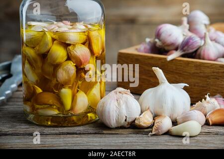 Aglio aromatico olio aromatizzato o bottiglia per infusione e casse di legno di spicchi di aglio in cucina in legno tavolo. Foto Stock