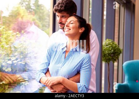 Ritratto di felice coppia giovane in piedi dalla finestra e godendo della reciproca compagnia mentre daydreaming. Foto Stock