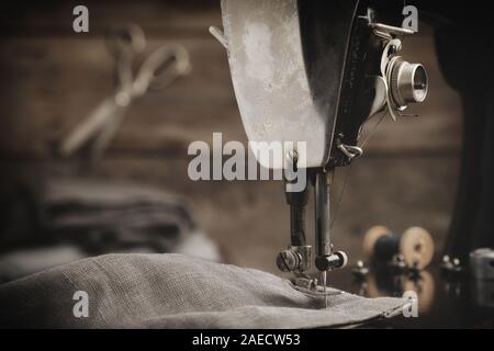 Antica macchina da cucire con un panno di lino. In fondo è appeso un sartoria forbici. Retrò workshop su misura. Foto Stock