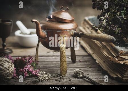 Antica teiera in ebollizione, secco coneflowers, vecchi libri e di erbe officinali. Foto Stock