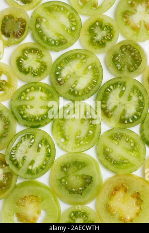 Solanum lycopersicum. Fette di acerbi, pomodori verdi su sfondo bianco. Foto Stock