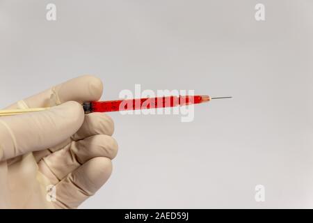 Medico tenendo la siringa riempita con fluido rosso Foto Stock