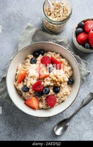 Ciotola di porridge di avena con frutti di bosco freschi mirtillo fragola e lampone. Tabella vista top shot, calcestruzzo o cemento sfondo Foto Stock