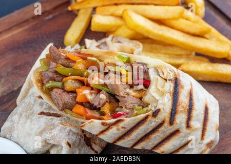 Tortilla avvolge i panini con verdure fresche, le carni macinate e servito con patate fritte sul bordo di taglio. Burrito, sandwich wrap, fajita wrap. Foto Stock