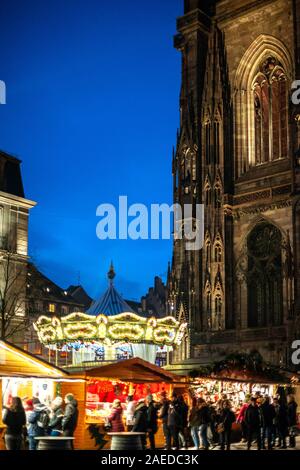 Strasburgo, Francia - Dic 20, 2016: l'immagine verticale scena notturna con fila di bancarelle del mercato chalets con più giocattoli e souvenir in vendita in Place de la Cathedrale e giostre giostra Foto Stock