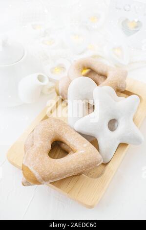 Biscotti di Natale di varie forme di zucchero a velo su di un bordo di taglio su un marrone tavolo in legno. Composizione di natale con pan di zenzero e teiera in bianco Foto Stock