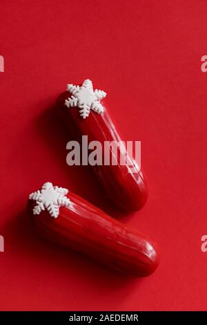 Rosso eclair vetrata con fiocchi di neve bianca in rosso sfondo colorato. Copyspace, flatlay, overhead, minimalismo alimentare il concetto di fotografia. Desser di natale Foto Stock