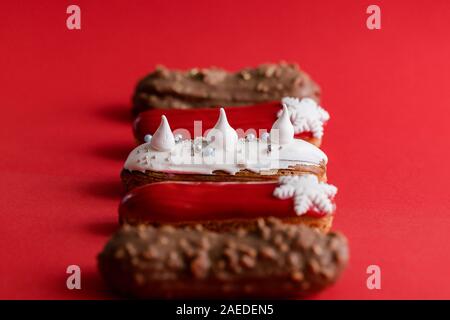 Rosso eclair vetrata con fiocchi di neve bianco su rosso sfondo colorato. Close up, minimalista alimentare il concetto di fotografia. Dolce di Natale Foto Stock