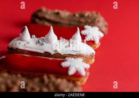 Rosso eclair vetrata con fiocchi di neve bianco su rosso sfondo colorato. Copyspace, close up, minimalista alimentare il concetto di fotografia. Dolce di Natale Foto Stock