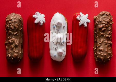 Rosso eclair vetrata con fiocchi di neve bianco su rosso sfondo colorato. Flatlay, overhead, minimalista alimentare il concetto di fotografia. Dolce di Natale Foto Stock