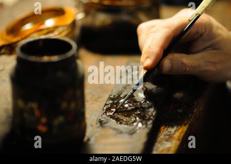 Maestro liutaio che vernicia un liuto a corde di violino fatto a mano come tocchi finali per completare la sua creazione nella sua officina a Cremona, Lombardia Foto Stock