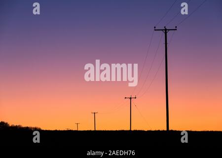 I tralicci elettrici National Grid che trasportano i cavi elettrici attraversano la campagna del Suffolk dopo il tramonto del sole invernale. Foto Stock