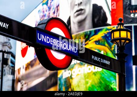 Metropolitana segno di entrata con la schermata di pubblicità in background a Piccadilly Circus, London, Regno Unito Foto Stock