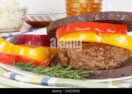 Salutari hamburger grigliato in salsa barbecue e servita su tostati Pane pumpernickel. E rabboccato con cotto giallo e peperoni rossi. Foto Stock