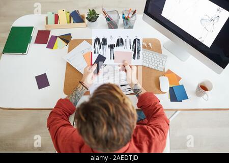 Vista sopra a tatuato maschio designer di moda disegno schizzi mentre la pianificazione progetto creativo al lavoro in studio o atelier, spazio di copia Foto Stock