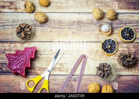 Sfondo di legno con tema natalizio. Ci sono rossi fiocchi e nastri, forbici, coni, dadi, candela in barca e una candela rossa come un albero di Natale. Foto Stock