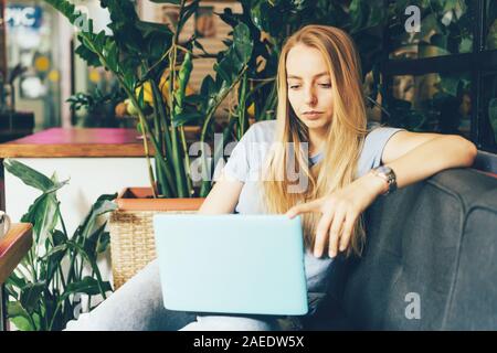 Giovane ragazza bionda manager in accoglienti coworking sul lettino con un laptop Foto Stock