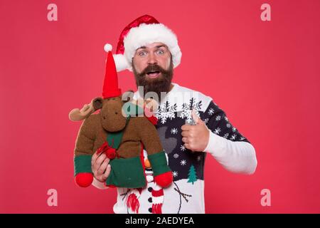 Babbi Natale cervi preferiti. Felice hipster dare simili con le renne giocattolo. Uomo Barbuto mostra pollice in alto come la mano. Come da Santa. Celebrare il Natale e il nuovo anno. Come se credere a Babbo Natale. Foto Stock