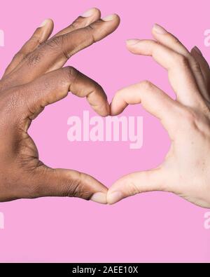 Cuore formato da mani African American caucasiche. Il concetto di diversità su sfondo rosa Foto Stock