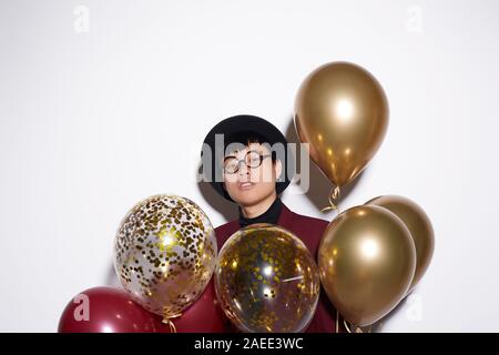Vita ritratto di moda uomo asiatico holding mazzetto di golden palloncini mentre posa contro uno sfondo bianco a parte, shot con flash, spazio di copia Foto Stock