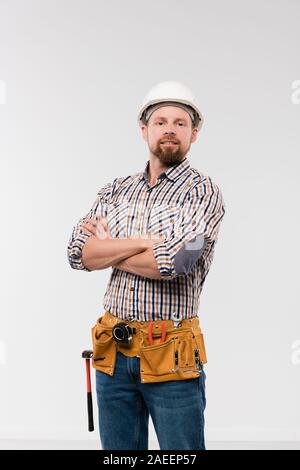 Giovane tecnico con toolbelt sulla sua vita attraversando le armi dal petto Foto Stock