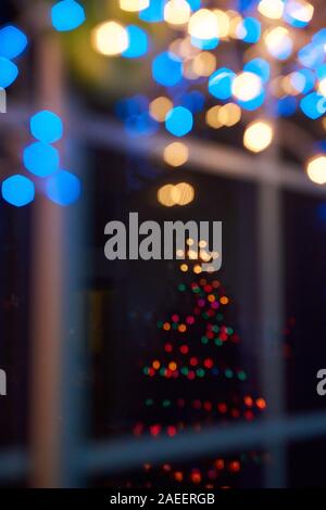 Al di fuori della messa a fuoco le luci di Natale appeso ad una finestra con riflessioni di un albero di Natale, scintillanti astratto dello sfondo. Foto Stock