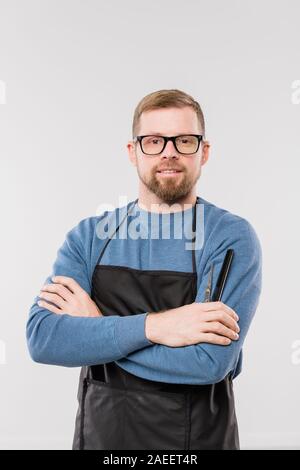 Giovani barbuto parrucchiere in grembiule blu e pullover in attesa per i clienti Foto Stock