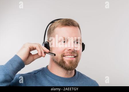 Giovani hotline barbuto operatore in cuffia e informale di client di consulenza Foto Stock