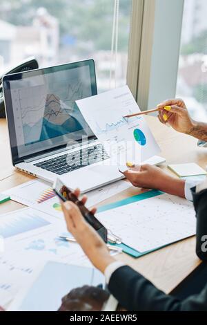Mani di dirigenti aziendali per discutere i dati finanziari sul documento cartaceo e lo schermo del notebook all'incontro Foto Stock