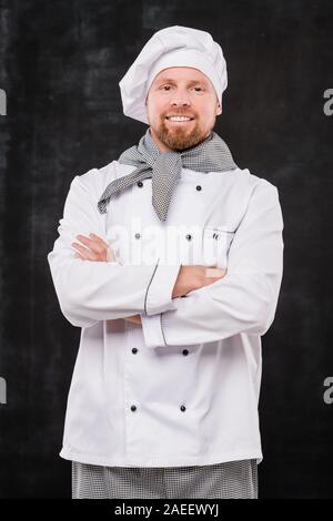 Giovane maschio sorridente chef bracci di attraversamento dal petto mentre guardando a voi Foto Stock