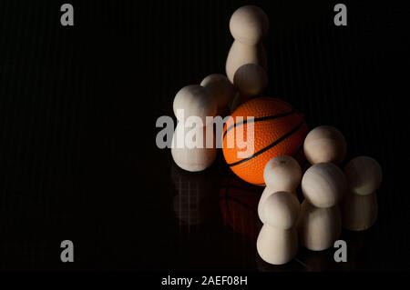 Pedine in legno e una palla da basket su uno sfondo nero. basket concept. Riprodurre il concetto. Foto Stock