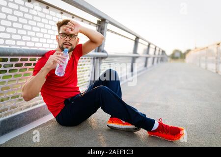 Esecuzione di maschio adulto prendendo una pausa. Stanco esaurito uomo runner sudorazione dopo allenamento cardio. Foto Stock