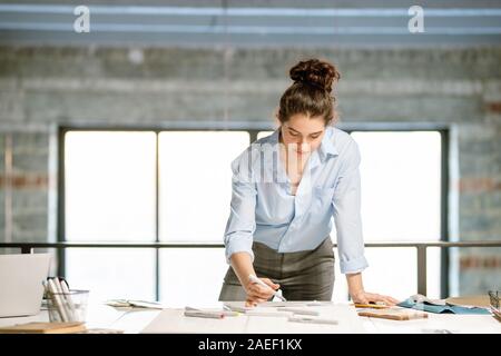 Giovane femmina grave flessione designer oltre la moda bozzetti sulla scrivania Foto Stock