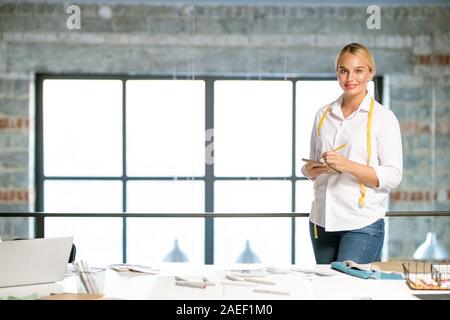 Bella femmina stilista di moda rendendo note o schizzo in notepad dal luogo di lavoro Foto Stock