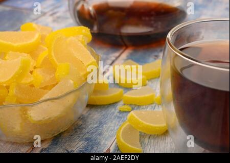 La marmellata di arance fette di limone, un bicchiere di tè nero e una teiera con infuso di tè su un sfondo di legno. Dolce con. Close up Foto Stock